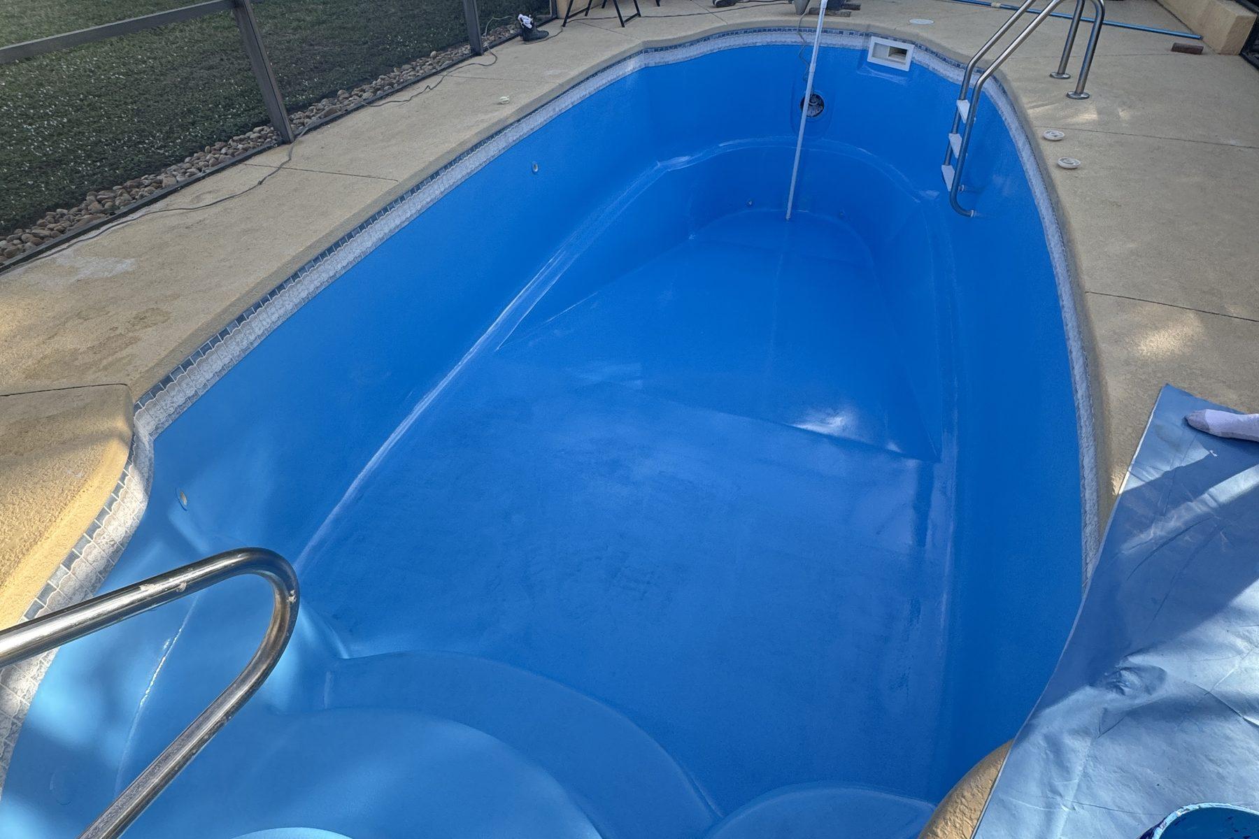 A drained bright blue fiberglass pool shell inside a screened enclosure, with a chrome handrail at the steps