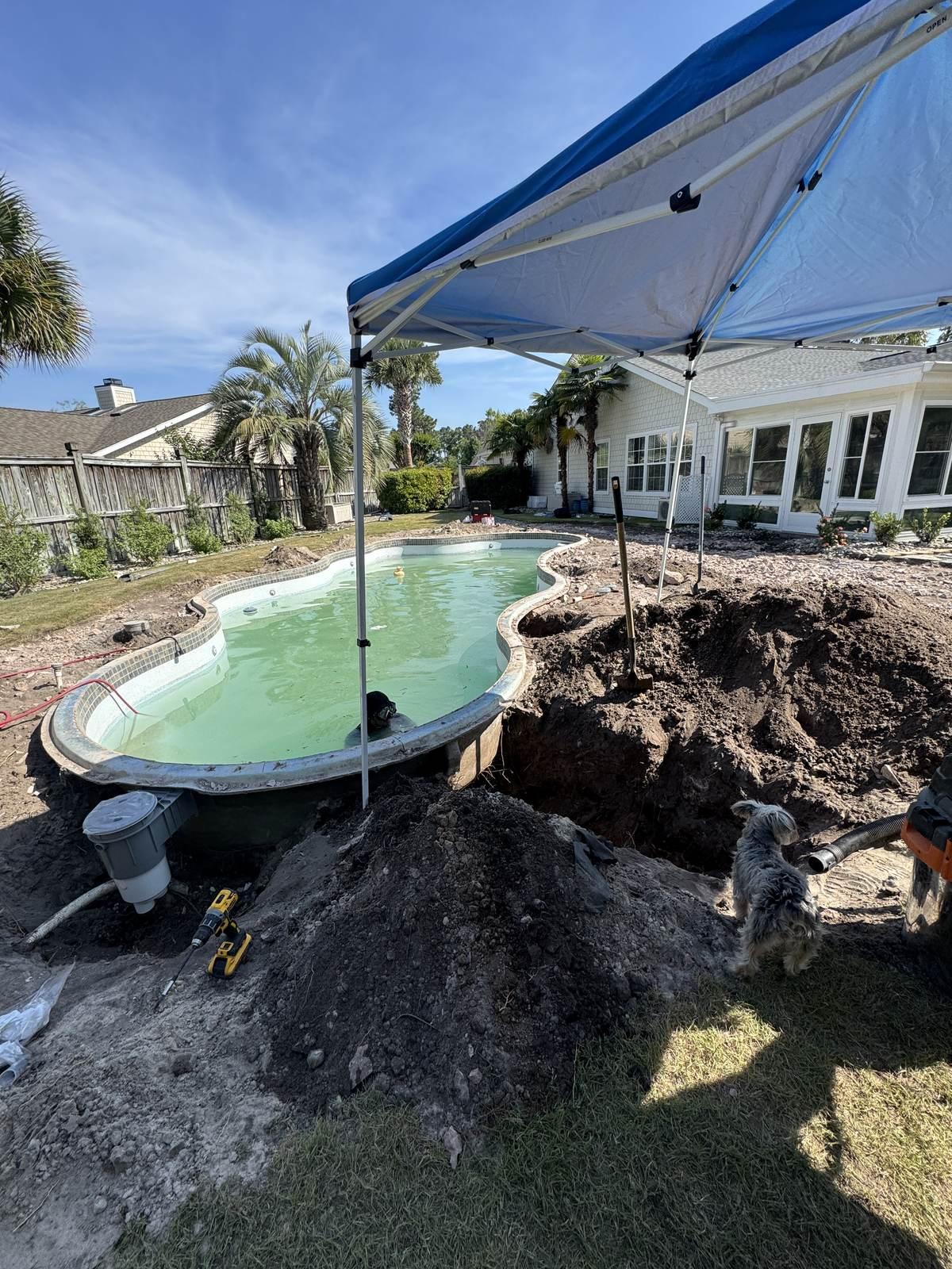 A pool with the deck edge excavated to reach the return lines, soil piled beside the opening, a work canopy over the dig and a skimmer housing in the foreground.