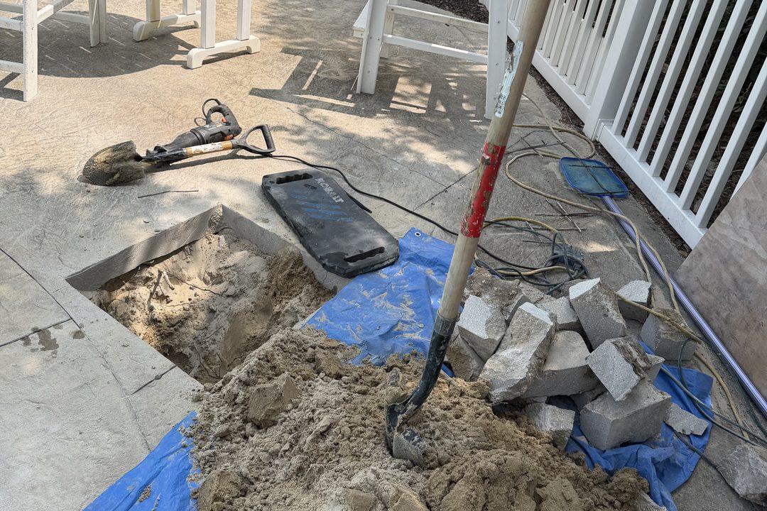 A small opened section of pool deck with neatly cut concrete blocks stacked on a tarp and a jackhammer set down